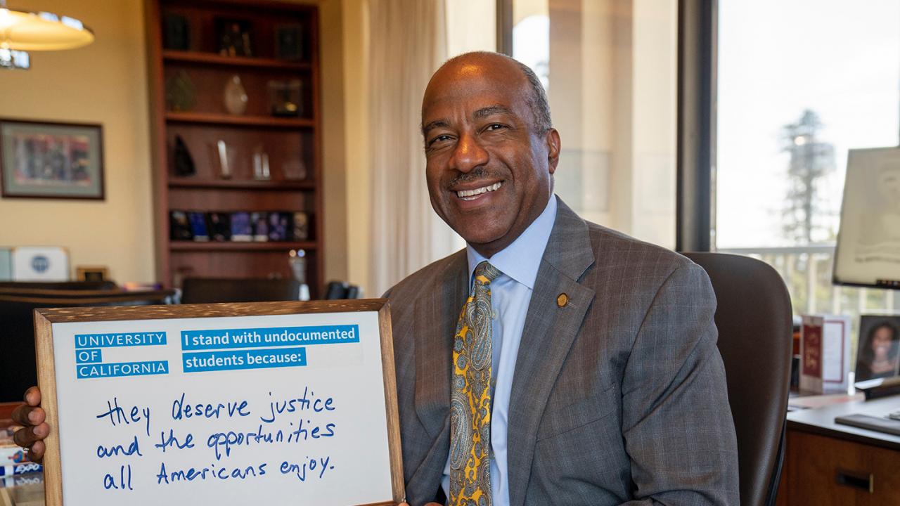 Photo of chancellor Gary S. May holding a white board that says "I stand with undocumented students because: They deserve justice and the opportunities all Americans enjoy."