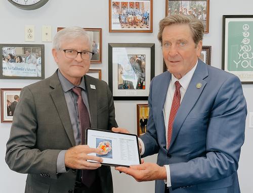 Left, white man in brown suite with white hair and glasses, on right taller white man with brown hair, blue suite and red tie.